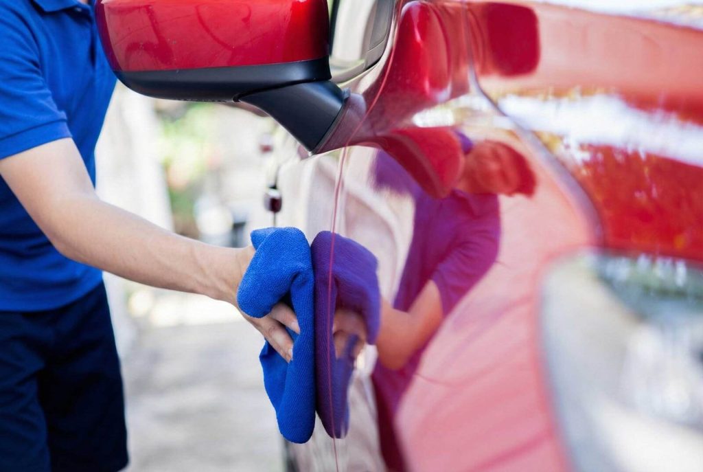 Mobile car detailing technician wiping red car exterior in Nashville apartment parking area